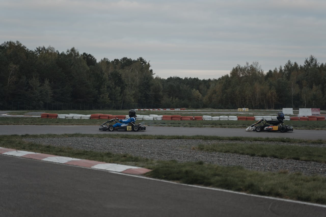 Two go-karts racing on an outdoor track surrounded by trees under a cloudy sky.