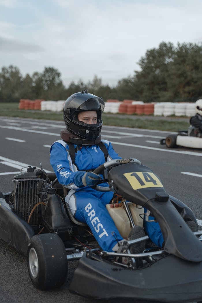 Young racer wearing protective gear in a go-kart on an outdoor racing track, ready to compete.
