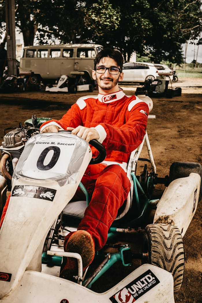 Portrait of a young man in a red racing suit sitting in a go-kart, smiling confidently outdoors.