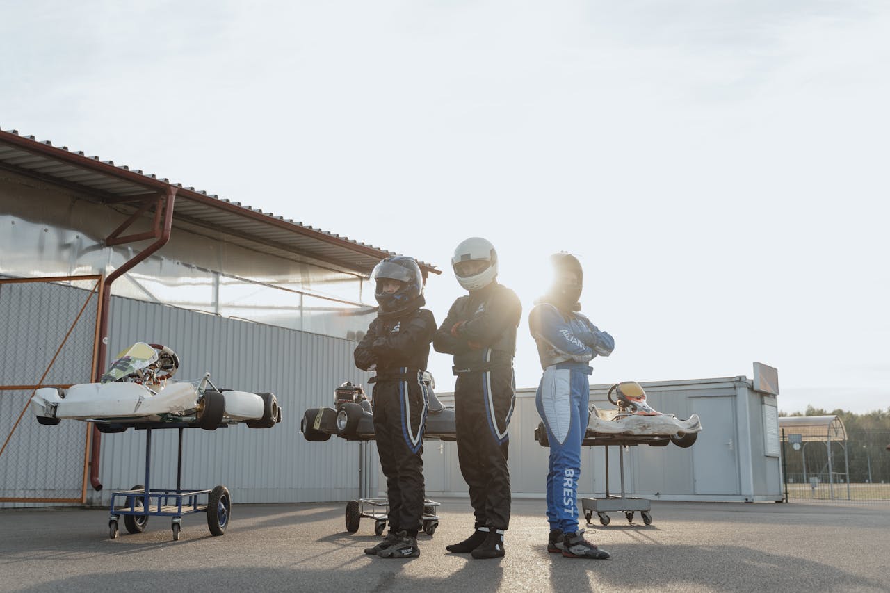 Three go-kart racers in helmets posing with their karts during sunset, showcasing motorsport spirit.