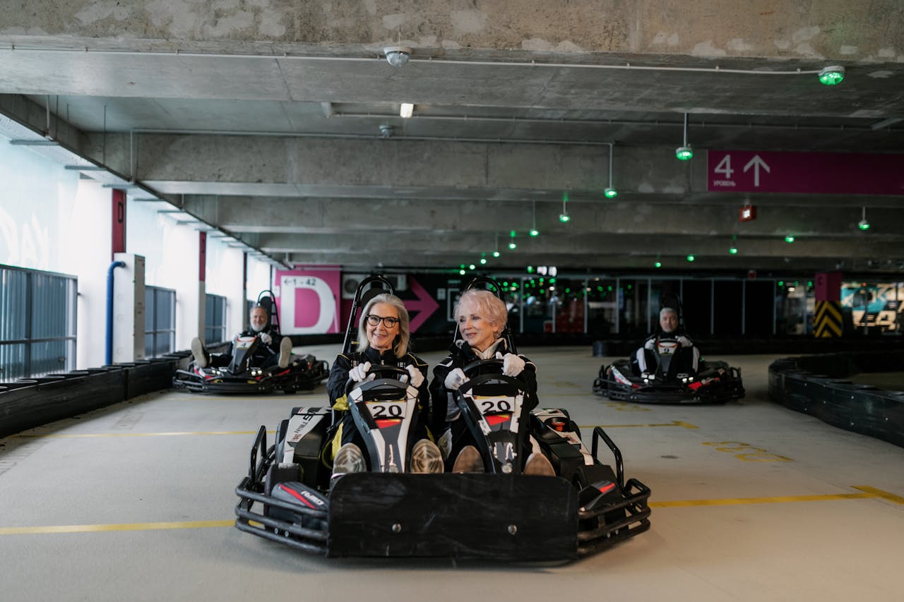 Elderly friends having fun racing go-karts indoors, enjoying recreational driving.